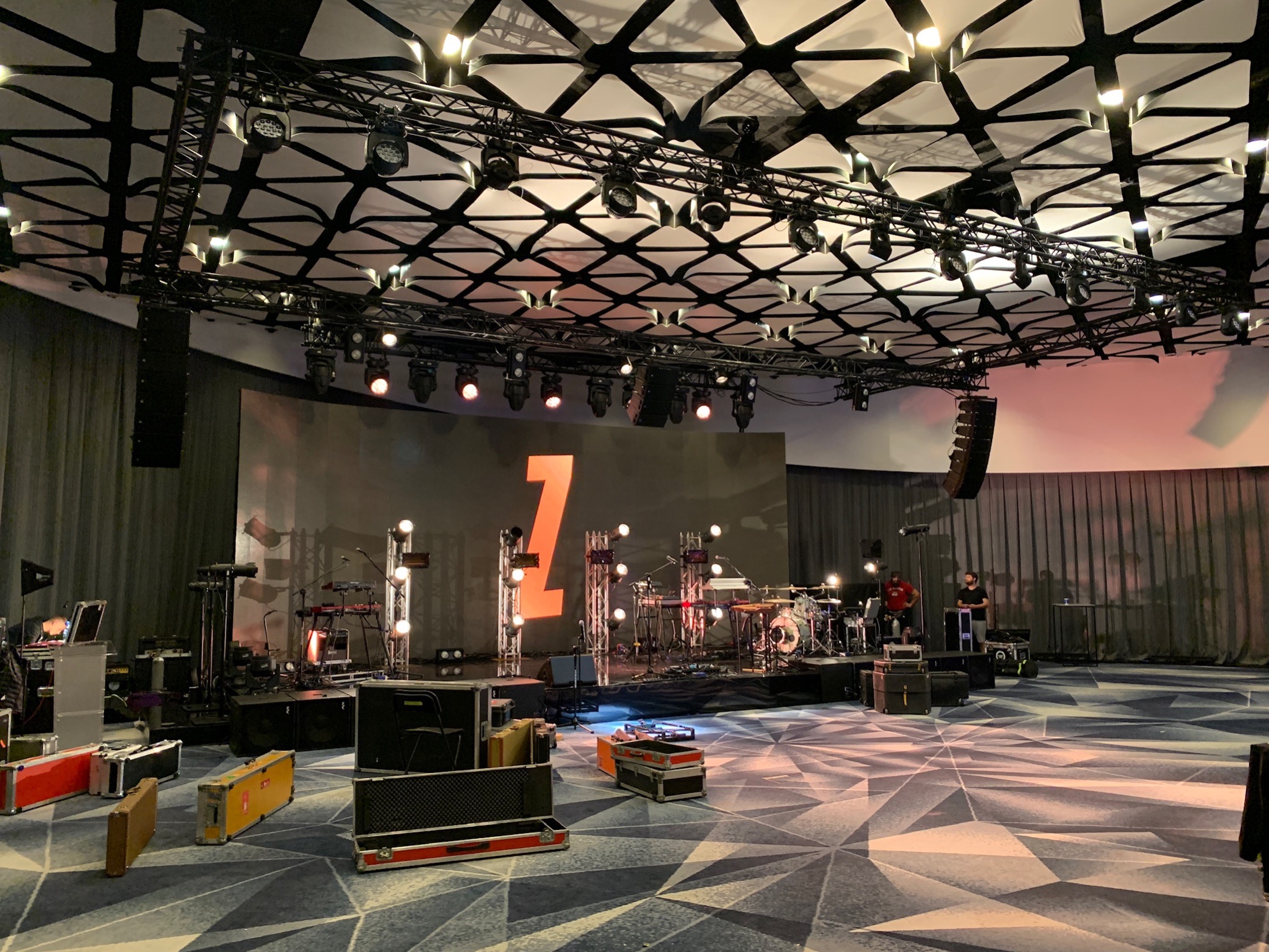 Przygotowania do koncertu w Lubawie: scena z instrumentami, oświetleniem i nagłośnieniem, widoczne skrzynie transportowe i obsługa techniczna.
