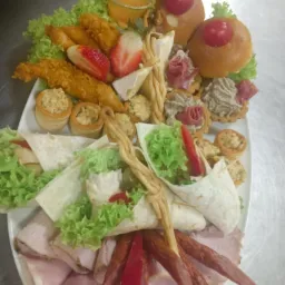 Elegancki półmisek z różnorodnymi przekąskami: tortille, koreczki, mięsa, owoce. Dekoracyjne ułożenie, widoczne detale, jasne kolory. Idealne na imprezę firmową.