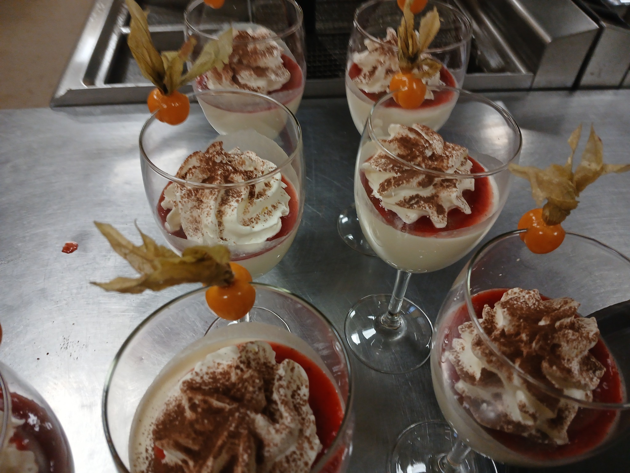 Eleganckie desery w szklanych pucharkach, udekorowane bitą śmietaną, kakao i physalis, gotowe do podania na przyjęciu. Widok z góry.