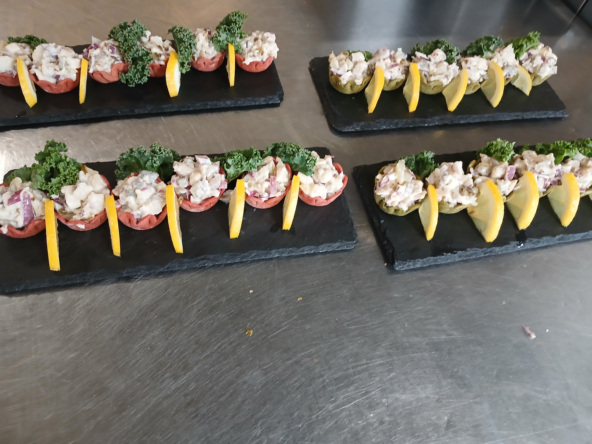 Elegancko podane przystawki na czarnych deskach: sałatka w kruchych babeczkach, udekorowana cytryną i zielonymi listkami, na metalowym blacie. Catering.