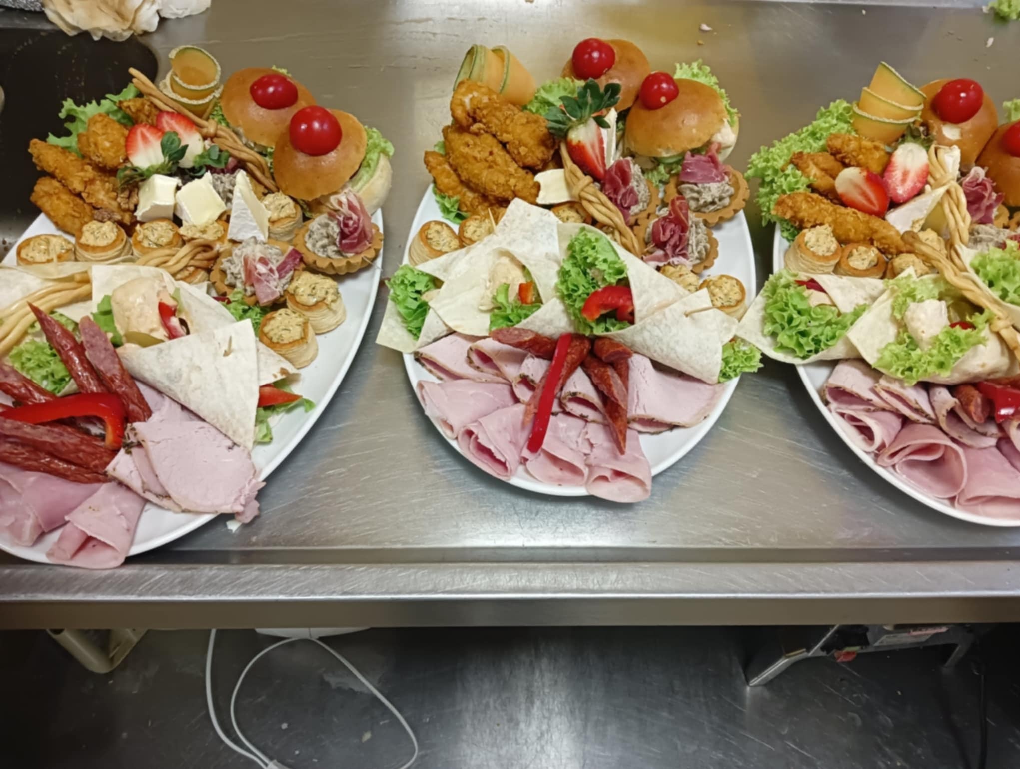Trzy talerze z różnorodnymi przekąskami: mini tortille, burgery z pomidorkami, wędliny, sery i sałatki. Idealne na catering firmowy lub przyjęcie okolicznościowe.