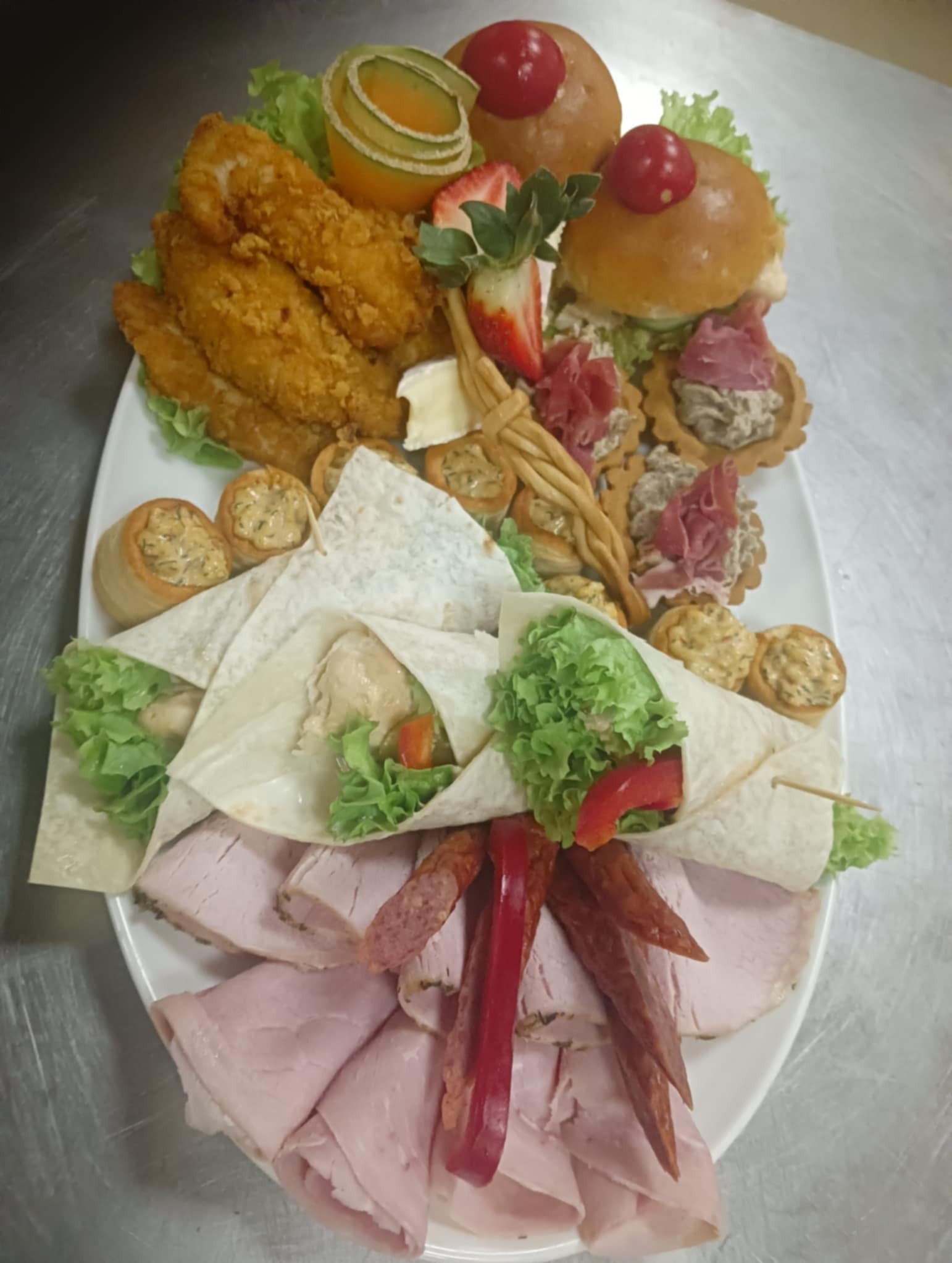 Elegancki, biały talerz z wyszukanymi przekąskami: mini tortille, burgery, roladki i wędliny, tworząc apetyczną kompozycję cateringową.