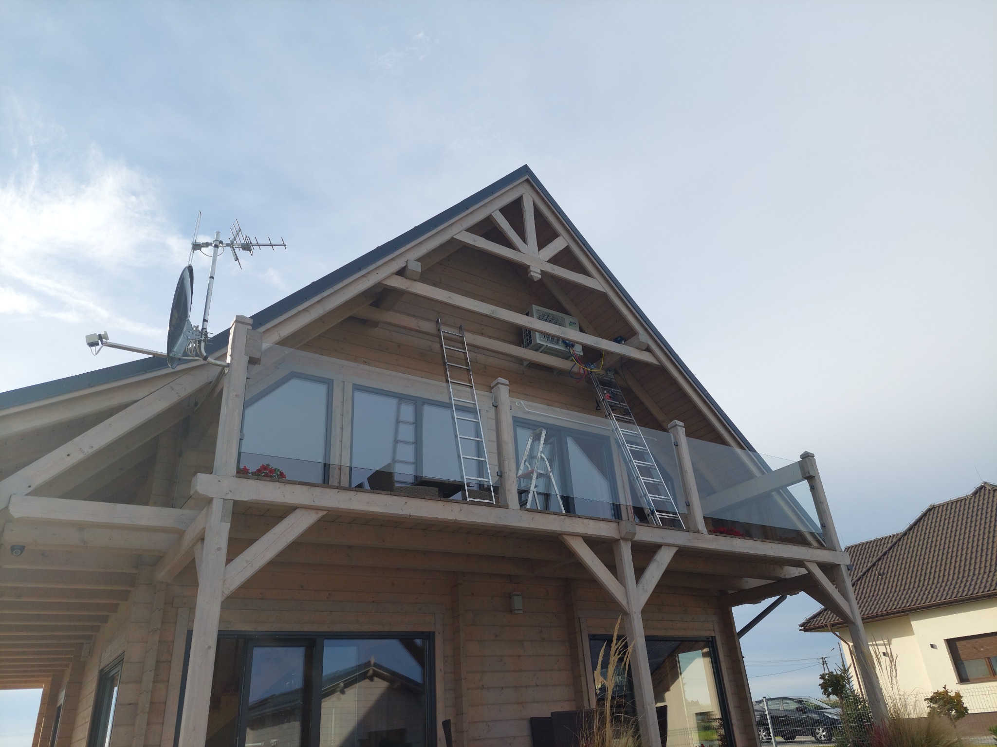 Drewniany dom z balkonem i klimatyzatorem na poddaszu, montaż za pomocą drabin opartych o elewację.