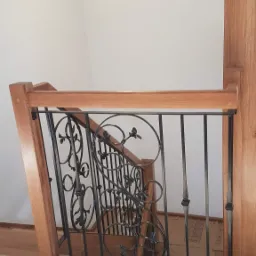 Kuta balustrada schodowa z drewnianymi elementami wykończeniowymi, widok z góry, oświetlona nowoczesną lampą sufitową.