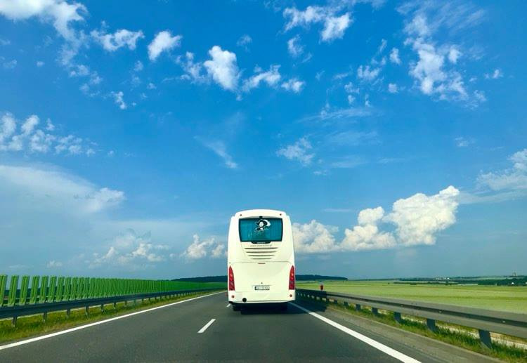 Biały autokar jadący autostradą w słoneczny dzień, widok z tyłu, z ekranem wyświetlającym animację na tylnej szybie.