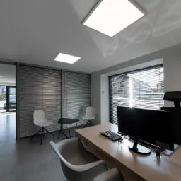 Jasne, minimalistyczne biuro z biurkiem, komputerem, krzesłami i żaluzjami, widok z szerokiego kąta, akcent na czystość i porządek.