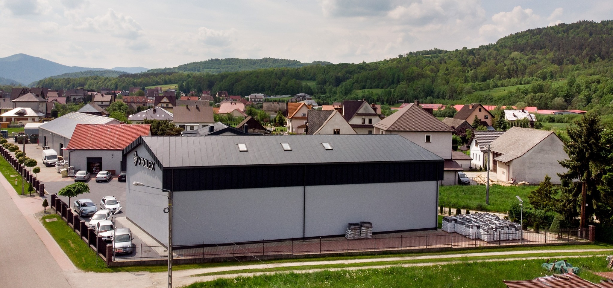 Widok z góry na magazyn firmy KROLEX z zapasem worków z produktami na zewnątrz, w tle zabudowa mieszkalna i zalesione wzgórza.