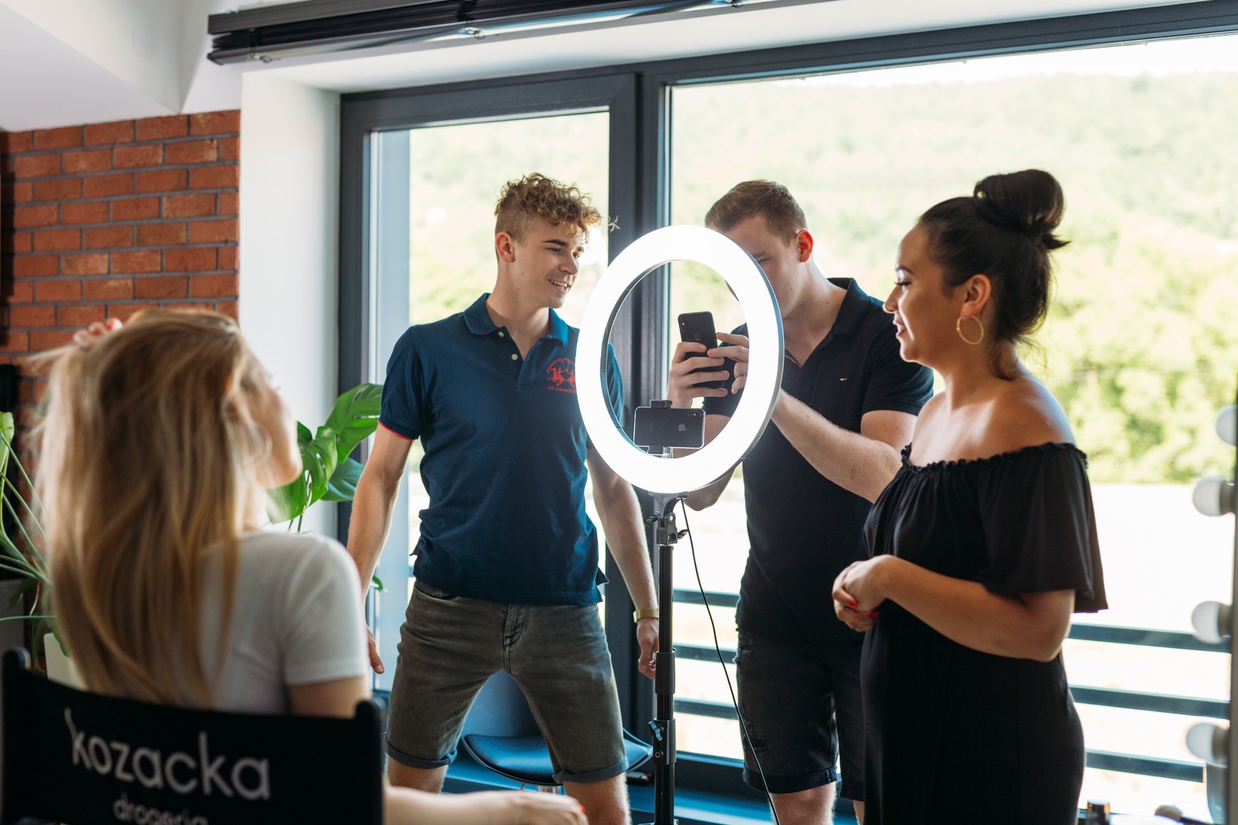 Sesja zdjęciowa z użyciem lampy pierścieniowej: mężczyzna fotografuje kobietę, drugi mężczyzna obserwuje.