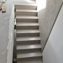 Schody wewnętrzne wykończone szarym mikrocementem, widok z góry na dół, z widocznymi śladami prac wykończeniowych na ścianach i podłodze.