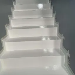 Białe schody pokryte błyszczącą powłoką, zabezpieczone taśmą malarską na krawędziach, widok z dołu w górę.