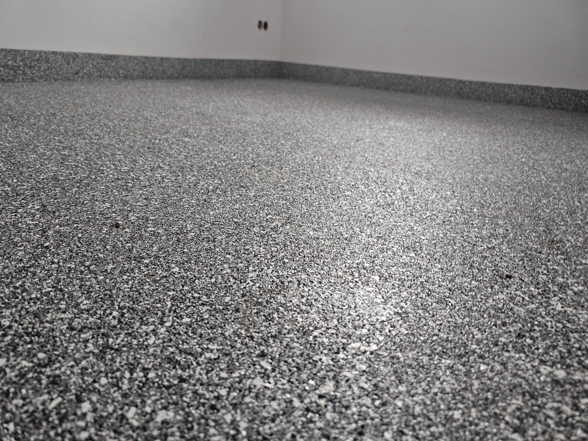 Szara, drobnoziarnista posadzka w pomieszczeniu w Otwocku, z widocznymi gniazdkami elektrycznymi przy ścianie, wykonana z bliska.