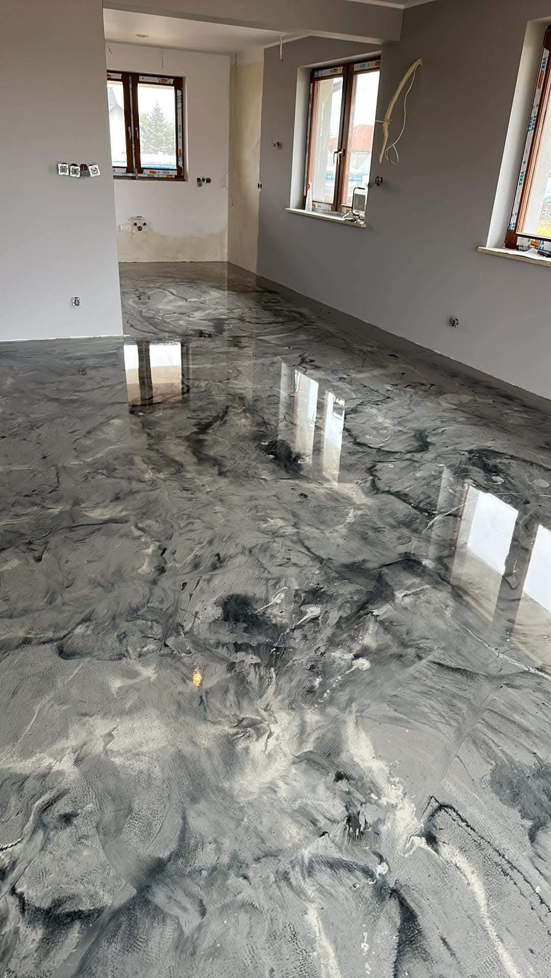 Błyszcząca, szara posadzka z efektem marmuru w jasnym, przestronnym wnętrzu z trzema oknami.
