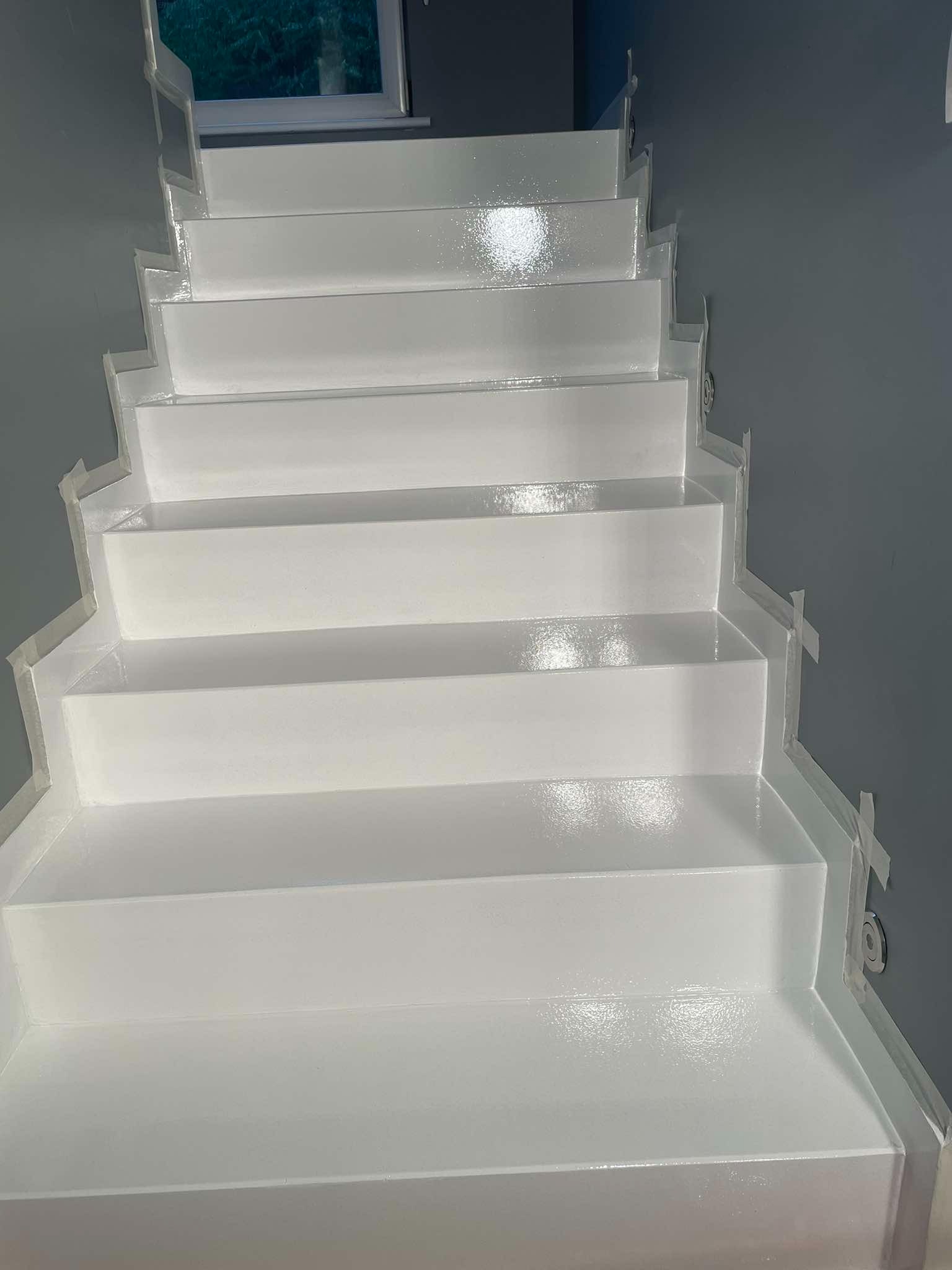 Białe schody pokryte błyszczącą powłoką, zabezpieczone taśmą malarską na krawędziach, widok z dołu w górę.