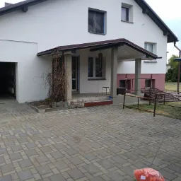 Dom jednorodzinny po świeżym malowaniu elewacji na biało, z widocznymi workami z odpadami budowlanymi na brukowanym podjeździe, okno zabezpieczone folią.