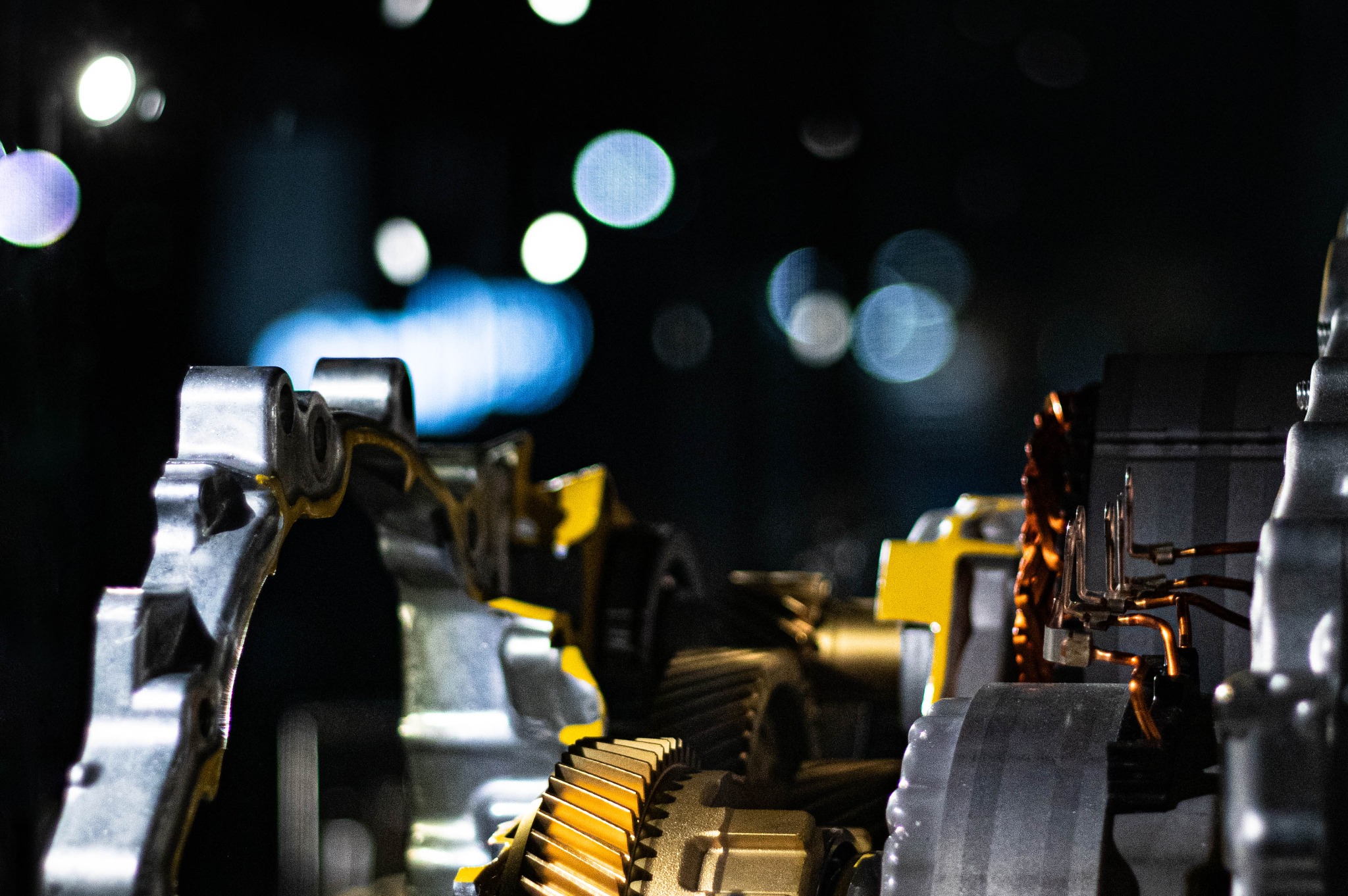 Przekrój skrzyni biegów maszyny z widocznymi zębatkami, elementami metalowymi i miedzianymi przewodami na rozmytym tle.