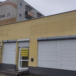 Bud-Walczak Mariusz Walczak - Żółta elewacja budynku z częściowo zdemontowanymi rusztowaniami, widoczne stare napisy i ogłoszenie o sprzedaży/wynajmie lokalu, osoba sprzątająca teren przed budynkiem.