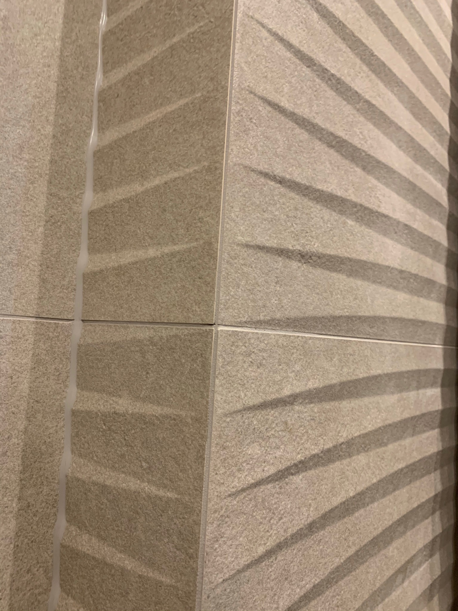 Fragment ściany wyłożonej beżowymi płytkami z trójwymiarowym wzorem, świeżo po fugowaniu, widoczne białe spoiny.