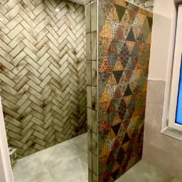 Wykończona łazienka z kabiną prysznicową oddzieloną ścianką z patchworkowych płytek w geometryczne wzory, ściana w strefie prysznica wyłożona jasną cegiełką ułożoną w jodełkę.