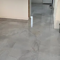 Błyszcząca, szara podłoga z płytek imitujących marmur w nowoczesnej kuchni z białą wyspą i sprzętami AGD.