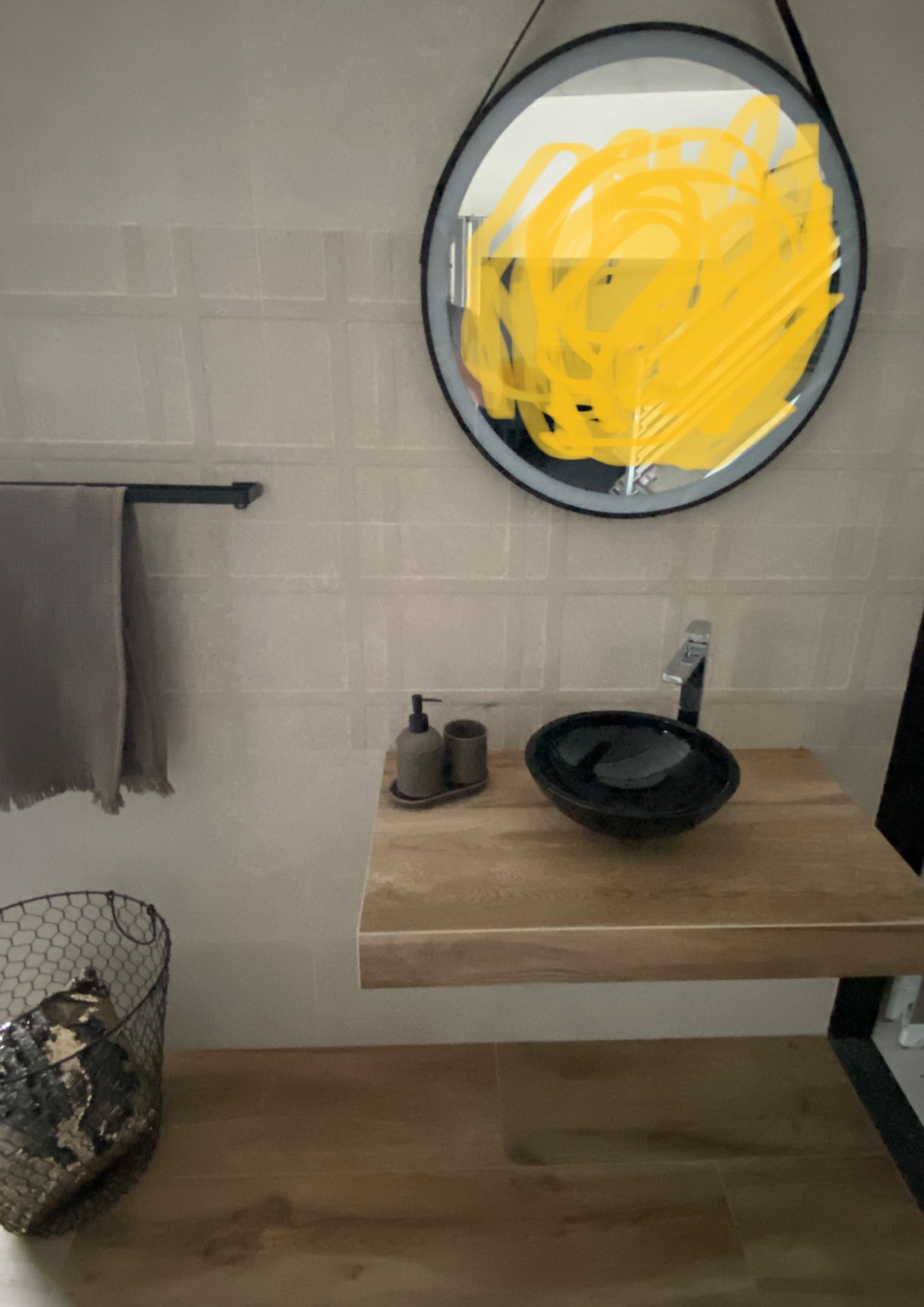 Nowoczesna łazienka z umywalką w kształcie misy, drewnianym blatem i okrągłym lustrem z czarną ramą; na ścianie widoczny ręcznik i dozownik mydła.