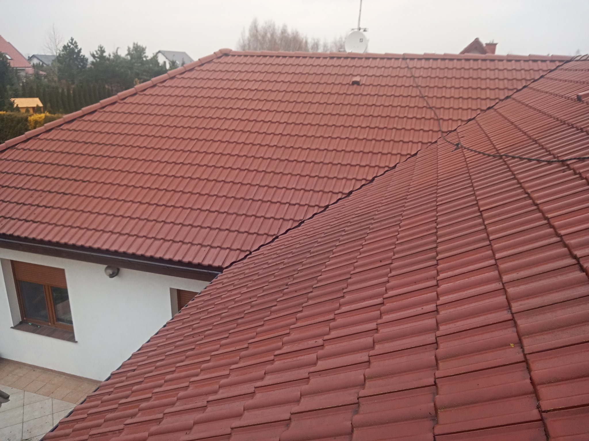 Nowy dach z czerwonej dachówki ceramicznej, widok z góry na dom z oknem z brązowymi roletami.