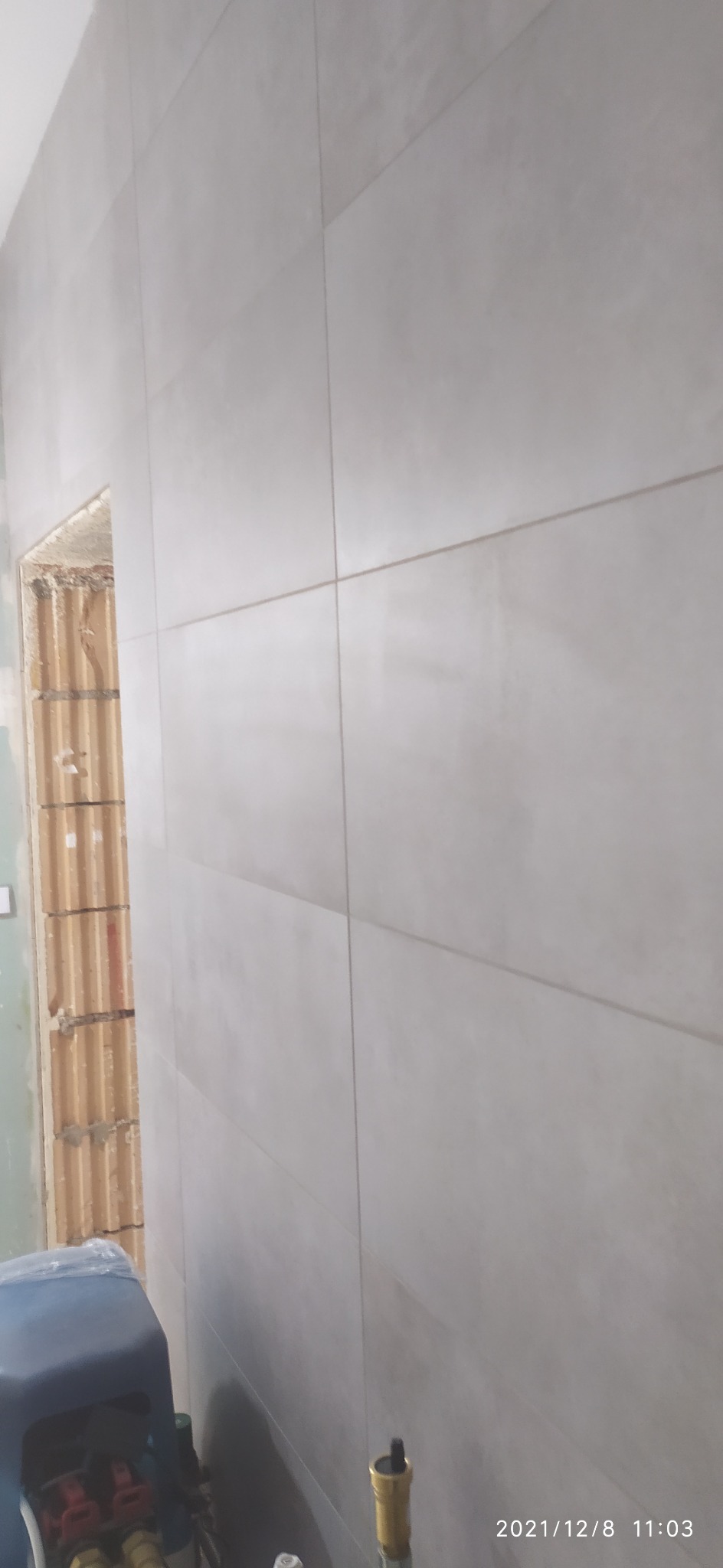 Ściana wyłożona jasnymi, prostokątnymi płytkami w trakcie remontu łazienki, widoczny fragment instalacji wodnej i fragment ściany z pustaków.