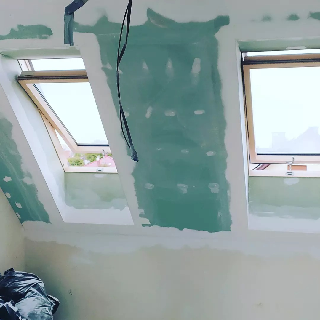 Poddasze w trakcie szpachlowania płyt gipsowo-kartonowych, widoczne okna dachowe i zwisający kabel.
