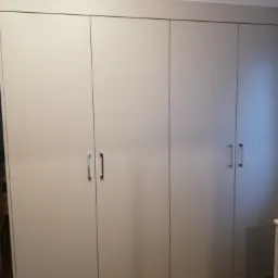 Pełna ściana zabudowana szafą z jasnymi, gładkimi frontami i metalowymi uchwytami, widoczna w mieszkaniu w Skierniewicach.