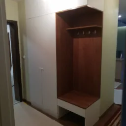 Wnęka z siedziskiem i wieszakami, stanowiąca część zabudowy szafy w przedpokoju, wykończona drewnem w ciepłym odcieniu.