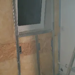 Montaż izolacji z wełny mineralnej w ścianie z oknem, widoczne metalowe profile i płyta OSB, etap prac wykończeniowych w pomieszczeniu.