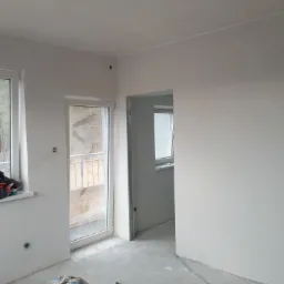 Wnętrze w Słupsku po gładziowaniu ścian i sufitu, widoczne narzędzia pracy: odkurzacz przemysłowy i worek z gładzią, przygotowane do dalszych prac wykończeniowych.