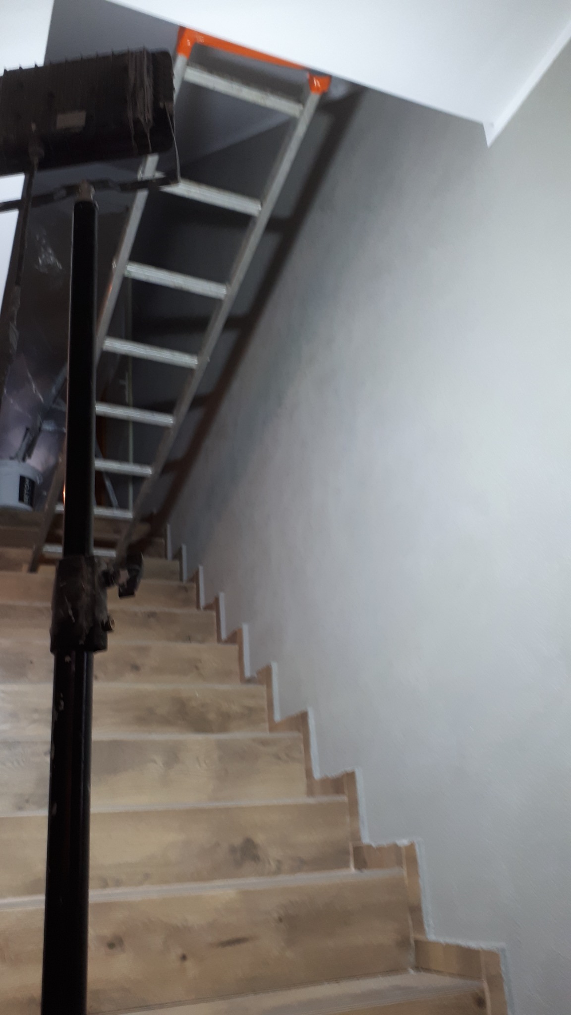 Schody drewniane w trakcie montażu, widoczna drabina i ściana przygotowana do malowania.
