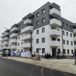 Nowoczesny budynek apartamentowy z balkonami zabezpieczonymi siatką, widok z ulicy w pochmurny dzień.