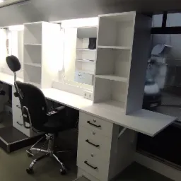 Wnętrze mobilnego salonu fryzjerskiego z białymi szafkami, lustrami z oświetleniem i czarnymi krzesłami fryzjerskimi, widok przez okno na zewnątrz.