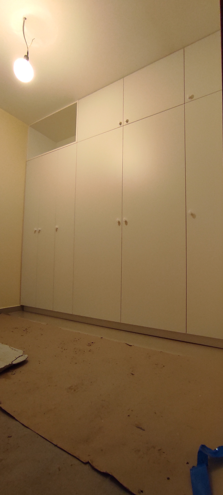 Biała zabudowa szafy wnękowej z okrągłymi uchwytami, widoczna na podłodze folia ochronna podczas montażu.