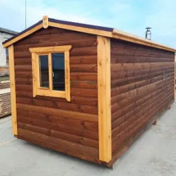 Gotowa, przenośna konstrukcja z ciemnego drewna z oknem z dekoracyjnymi detalami, prawdopodobnie przeznaczona na małą saunę.