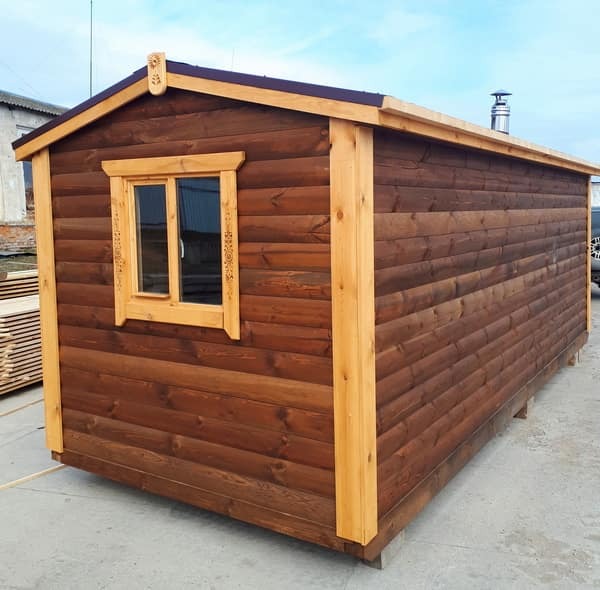 Gotowa, przenośna konstrukcja z ciemnego drewna z oknem z dekoracyjnymi detalami, prawdopodobnie przeznaczona na małą saunę.