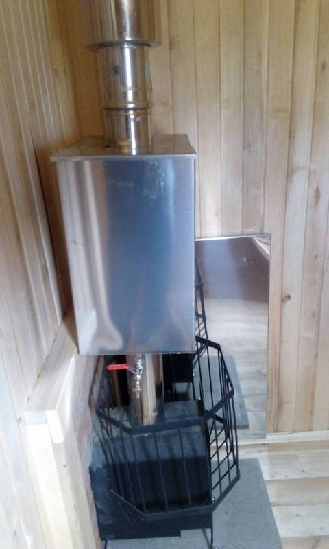 Metalowy piec do z drewnianą obudową, z czarnym, metalowym koszem ochronnym, widoczny wewnątrz pomieszczenia z boazerią.