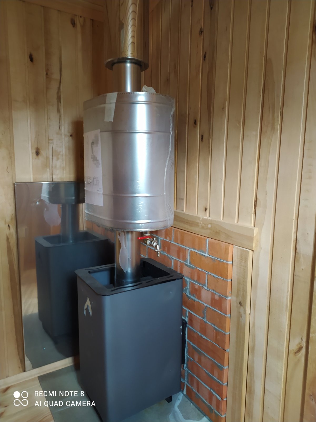 Wnętrze kabiny z piecem opalanym drewnem, kominem obłożonym folią ochronną, obudowa z cegieł, drewniane panele ścienne.