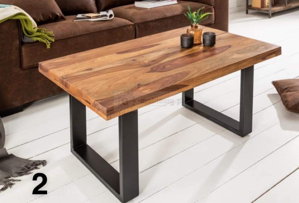 Stolik kawowy z blatem z egzotycznego drewna i czarnymi metalowymi nogami w kształcie litery U, na tle brązowej sofy i białej podłogi z desek.