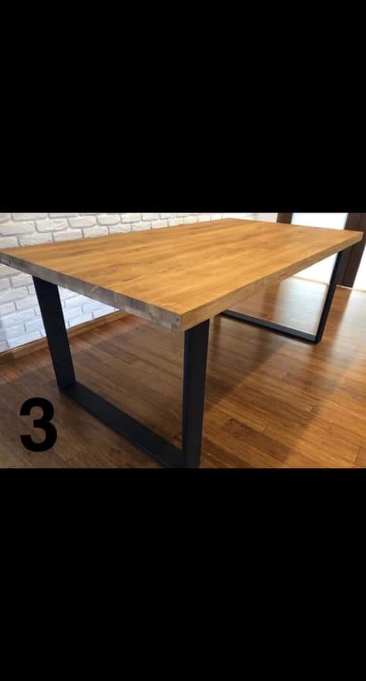 Stół z blatem z jasnego drewna i czarnymi, metalowymi nogami w kształcie litery U, ustawiony na drewnianej podłodze, z widoczną ścianą z białej cegły w tle.