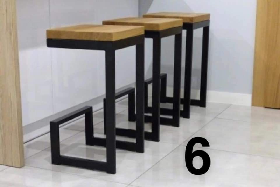 Trzy identyczne, nowoczesne stołki barowe z drewnianymi siedziskami i czarnymi, metalowymi nogami o kwadratowym przekroju, ustawione jeden za drugim na jasnej, błyszczącej podłodze.