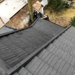 Prace dekarskie w Kosowie Lackim: Dwóch dekarzy montuje czarne dachówki bitumiczne na dachu domu, widok z góry.