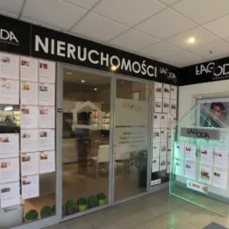 Wejście do biura nieruchomości Lagoda z plakatem oferty na ścianie i podświetlaną, przezroczystą makietą domu z ofertami, zieleń w doniczkach przy drzwiach.