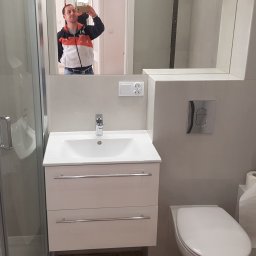 Profesjonalne wykańczanie wnętrz - Nowoczesna łazienka z kabiną prysznicową, umywalką z szafką i toaletą, odbicie fotografa w lustrze.