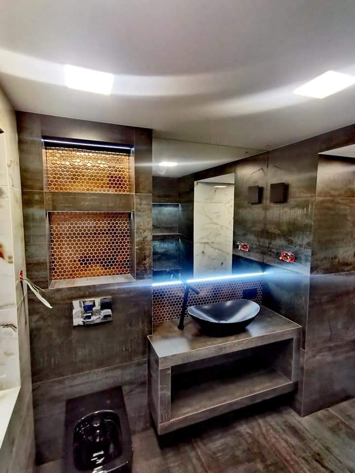 Nowoczesna łazienka z ciemnymi płytkami imitującymi rdzę, umywalką nablatową w kształcie misy i dekoracyjną mozaiką w niszach ściennych podświetlonych ledami.