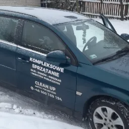 Granatowy samochód kombi z otwartymi drzwiami w zimowej scenerii, na karoserii biały napis 'Kompleksowe Sprzątanie: biur, domów, mieszkań, obiektów publicznych. Clean Up, Aneta Tokarczuk +48 500...