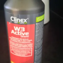 Butelka środka czyszczącego Clinex W3 Active Shield na ciemnym blacie, w tle rolka papieru.