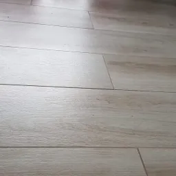 Ułożone panele podłogowe o jasnym odcieniu drewna, widoczne z bliska, z delikatną fakturą i subtelnymi spoinami.