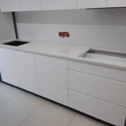 Biały blat kuchenny z wyciętymi otworami na zlew i płytę grzewczą, widoczne puszki instalacyjne na ścianie, minimalistyczny styl.